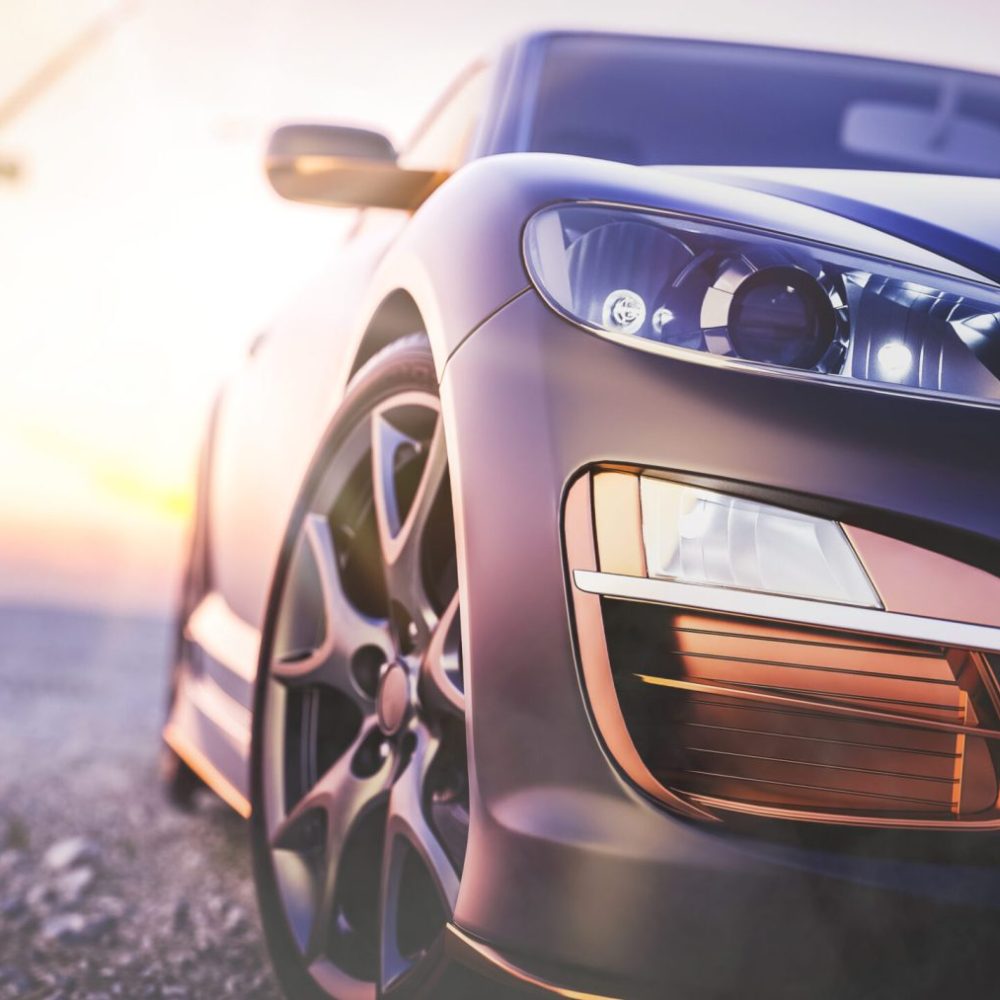 The image in front of the sports car scene behind as the sun going down with wind turbines in the back.