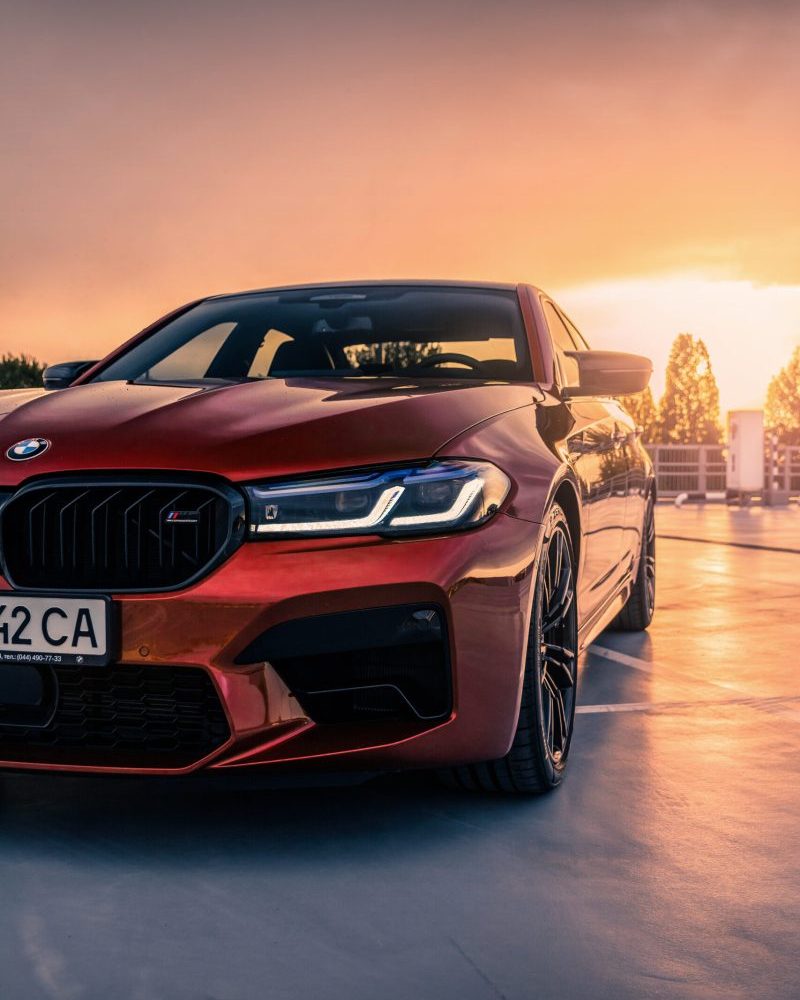 New BMW M5 F90 LCI Competition in a red color on the empty parking lot at sunset.